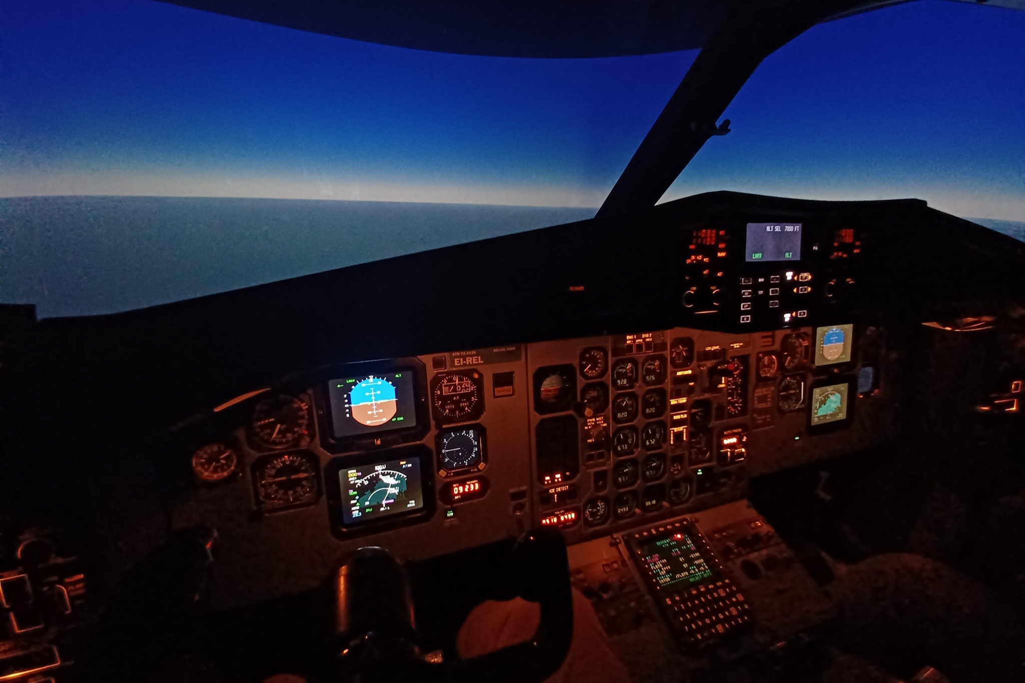 Alacakaranlıkta boş bir ATR-72 simülatör kokpiti; göstergeler yanıyor, camın ardında simüle edilmiş bir ufuk çizgisi var.