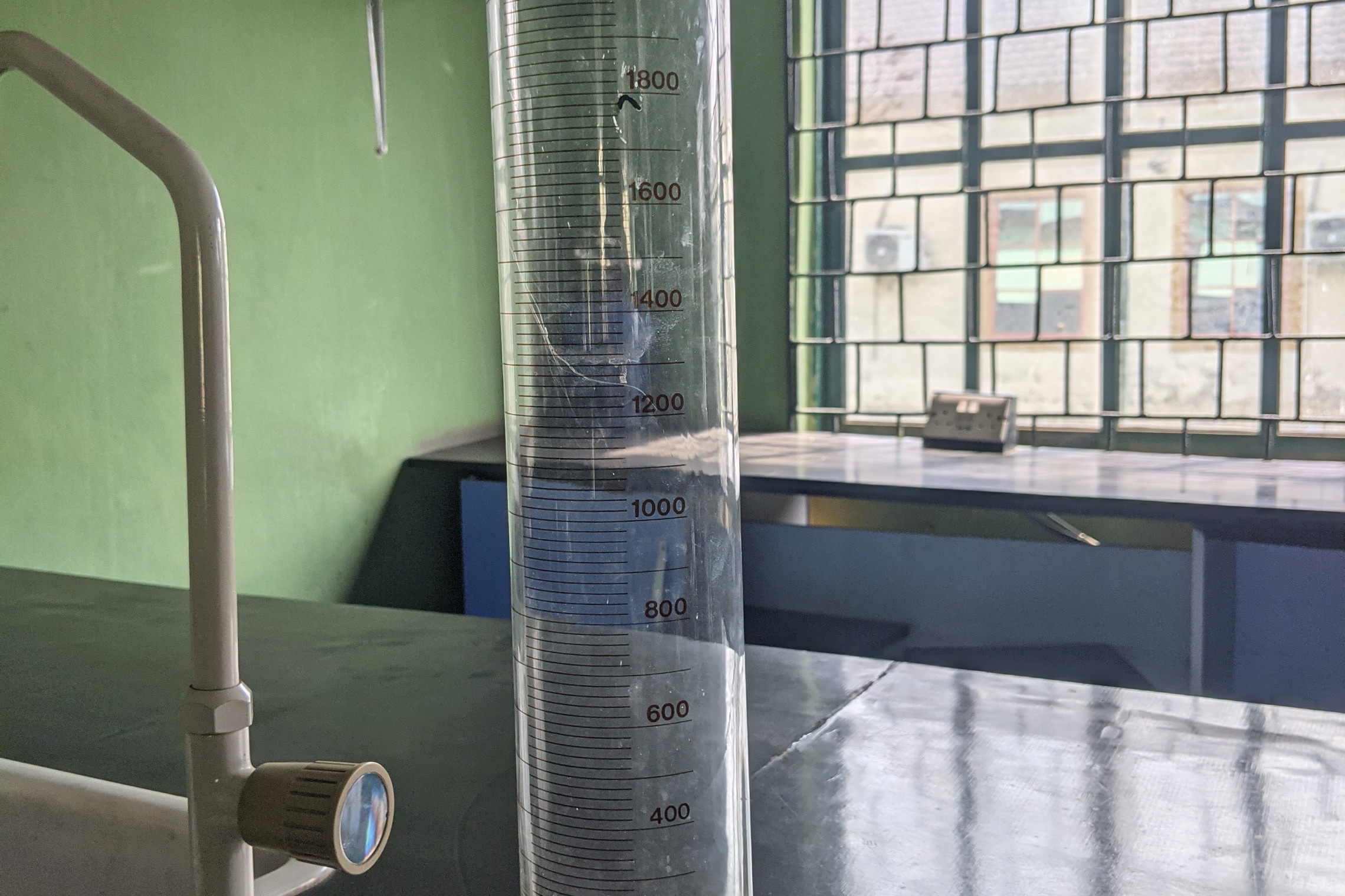 Laboratuvar tezgâhında duran dereceli büyük bir cam silindir; sıvı seviyesi mililitre çizgilerinin ortasında.